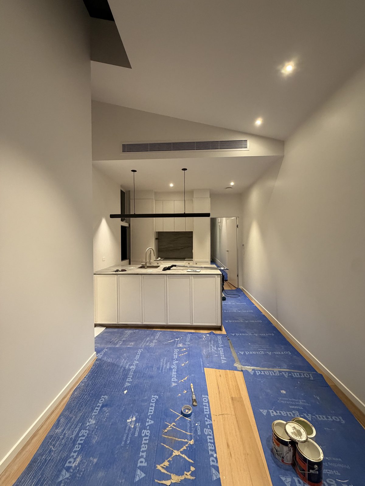 Same kitchen and living area before the clean, with blue protective floor covering over the timber floor and paint tins sitting on the covered floor
