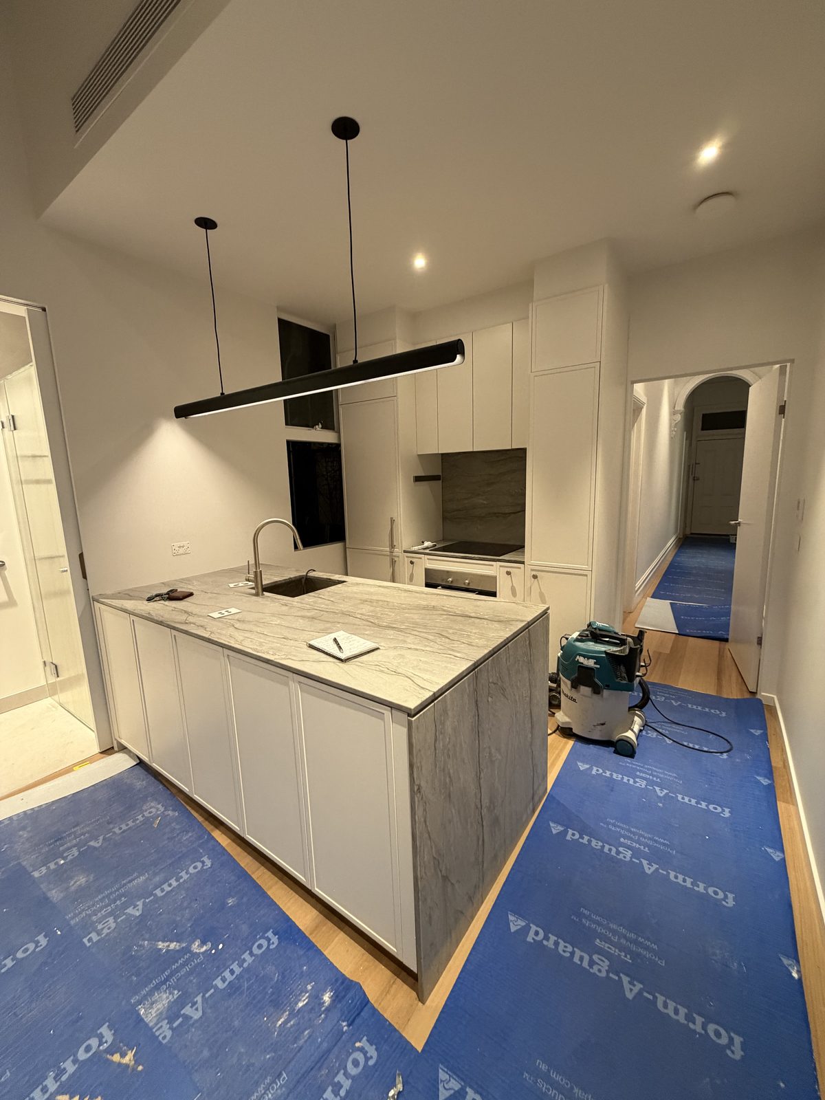 Kitchen island from the side with a dust extraction vacuum on the protected floor, before the timber flooring was uncovered