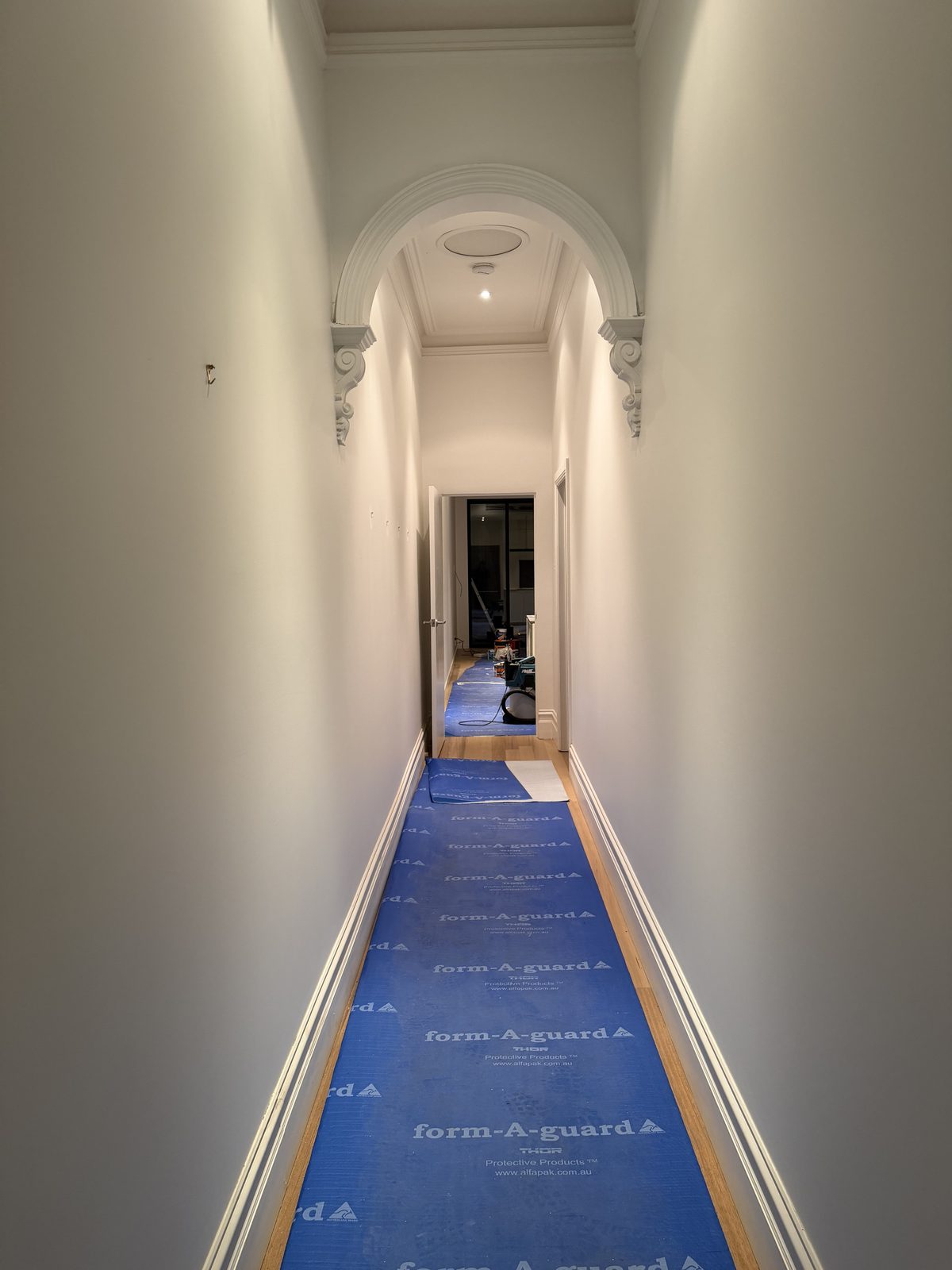 Period hallway with arched opening and corbels during the build, timber floor covered in blue protective sheeting ahead of the handover clean