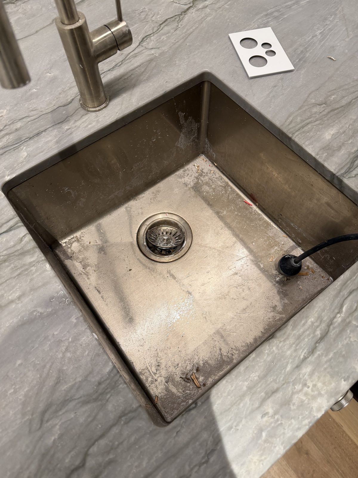 Undermount stainless steel sink coated in plaster dust and construction residue before cleaning, set in a marble-look stone benchtop