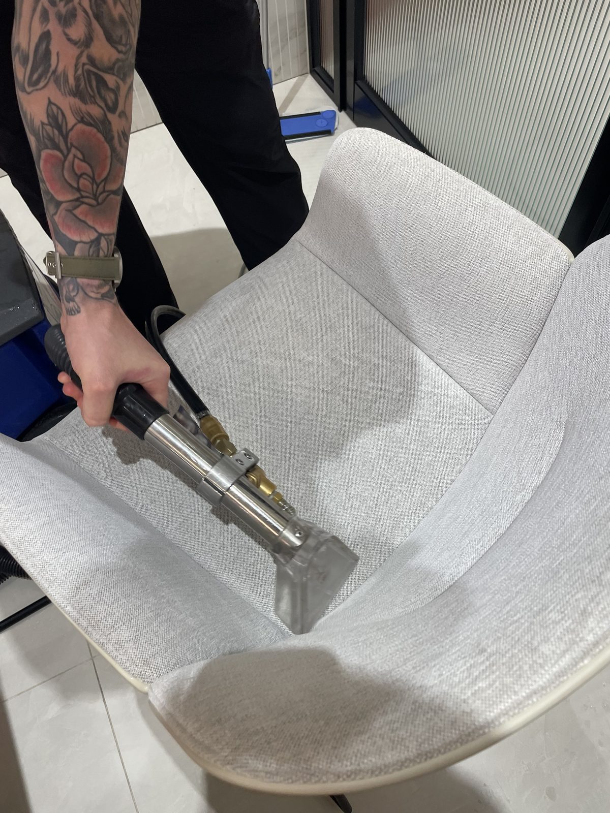 Close-up of a steam extraction wand cleaning the seat of a light grey upholstered chair