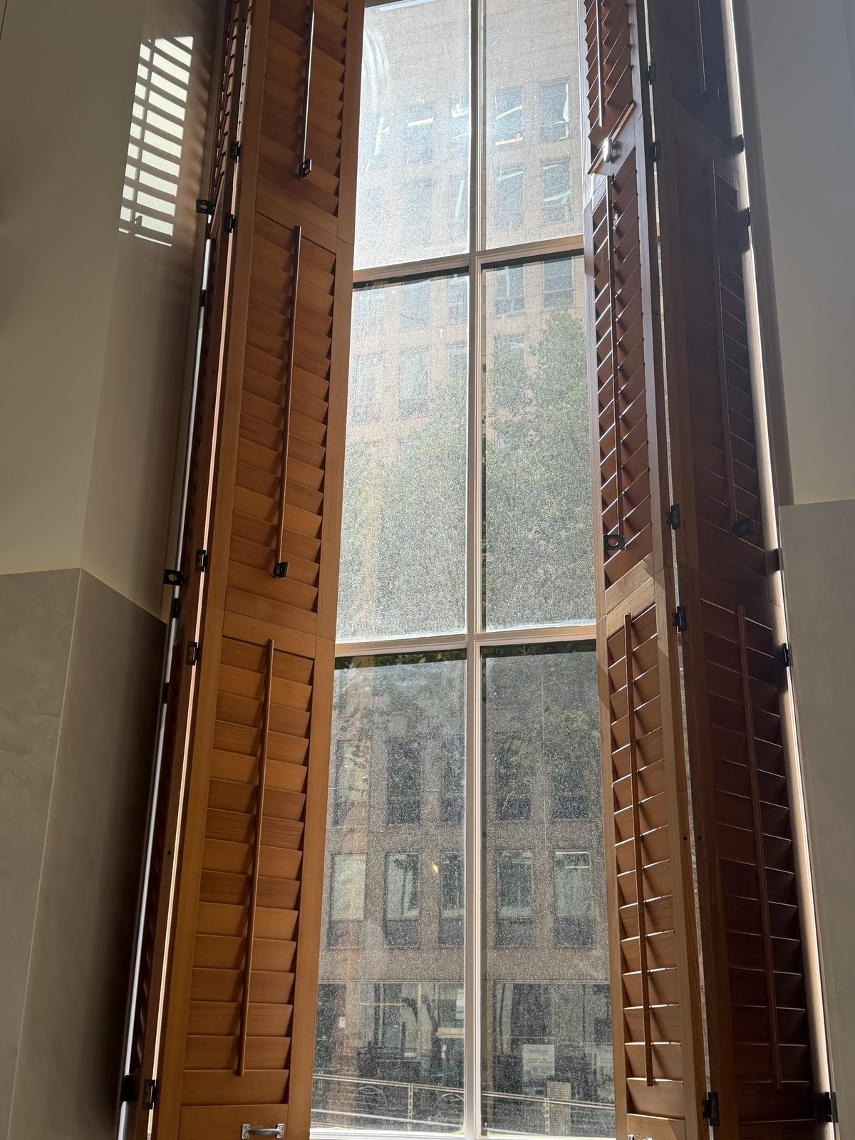 Tall multi-pane window with timber shutters, the glass visibly hazy and covered in spots and water marks