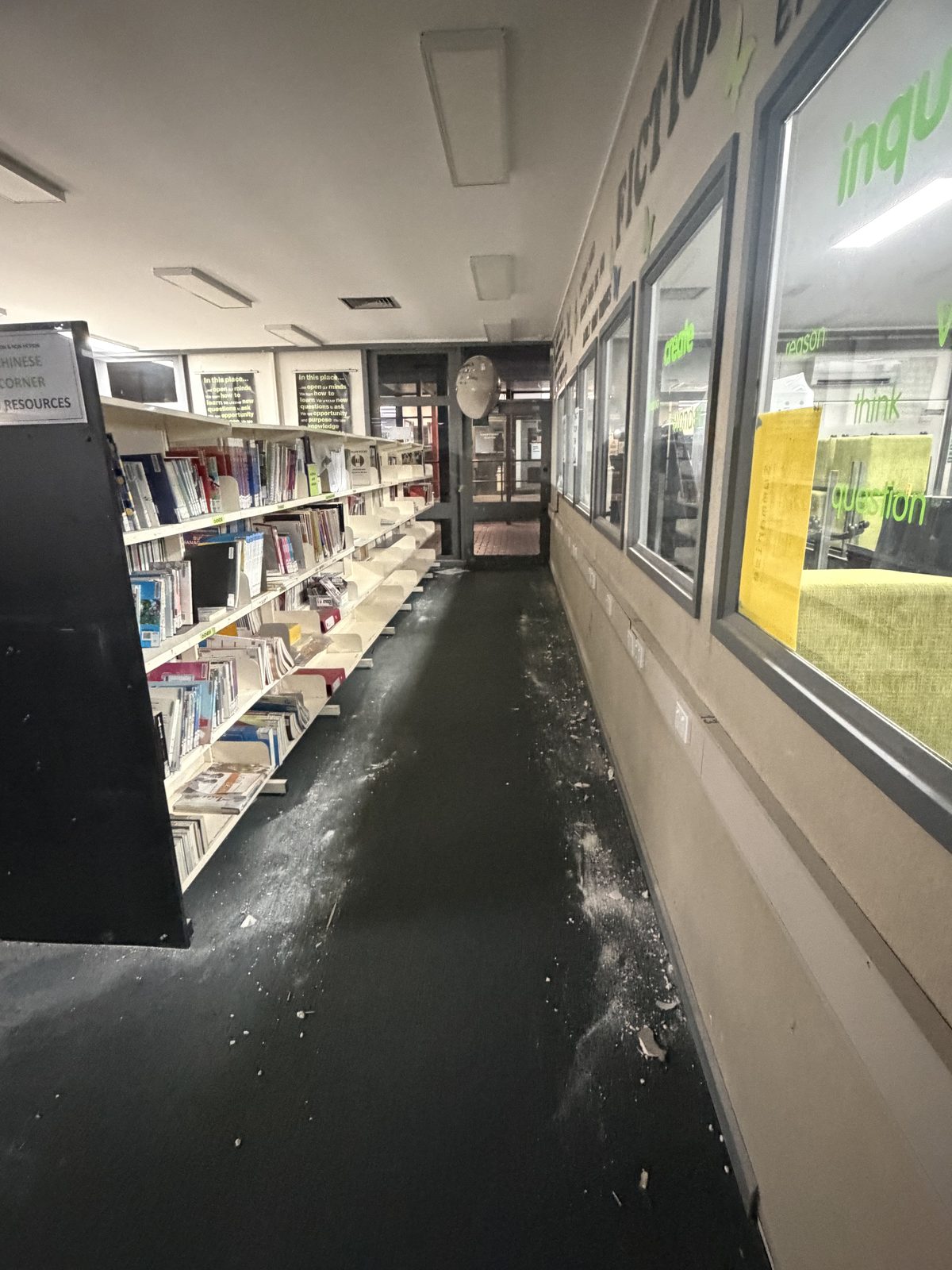 Plaster debris and dust scattered over dark carpet along a window-lined library walkway after plaster works