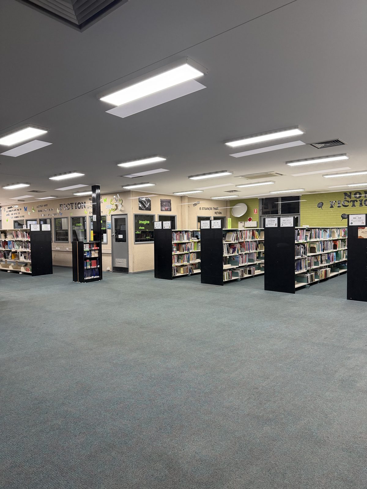 Wide view of the finished library with uniformly clean green carpet and stocked shelving after the end of build clean