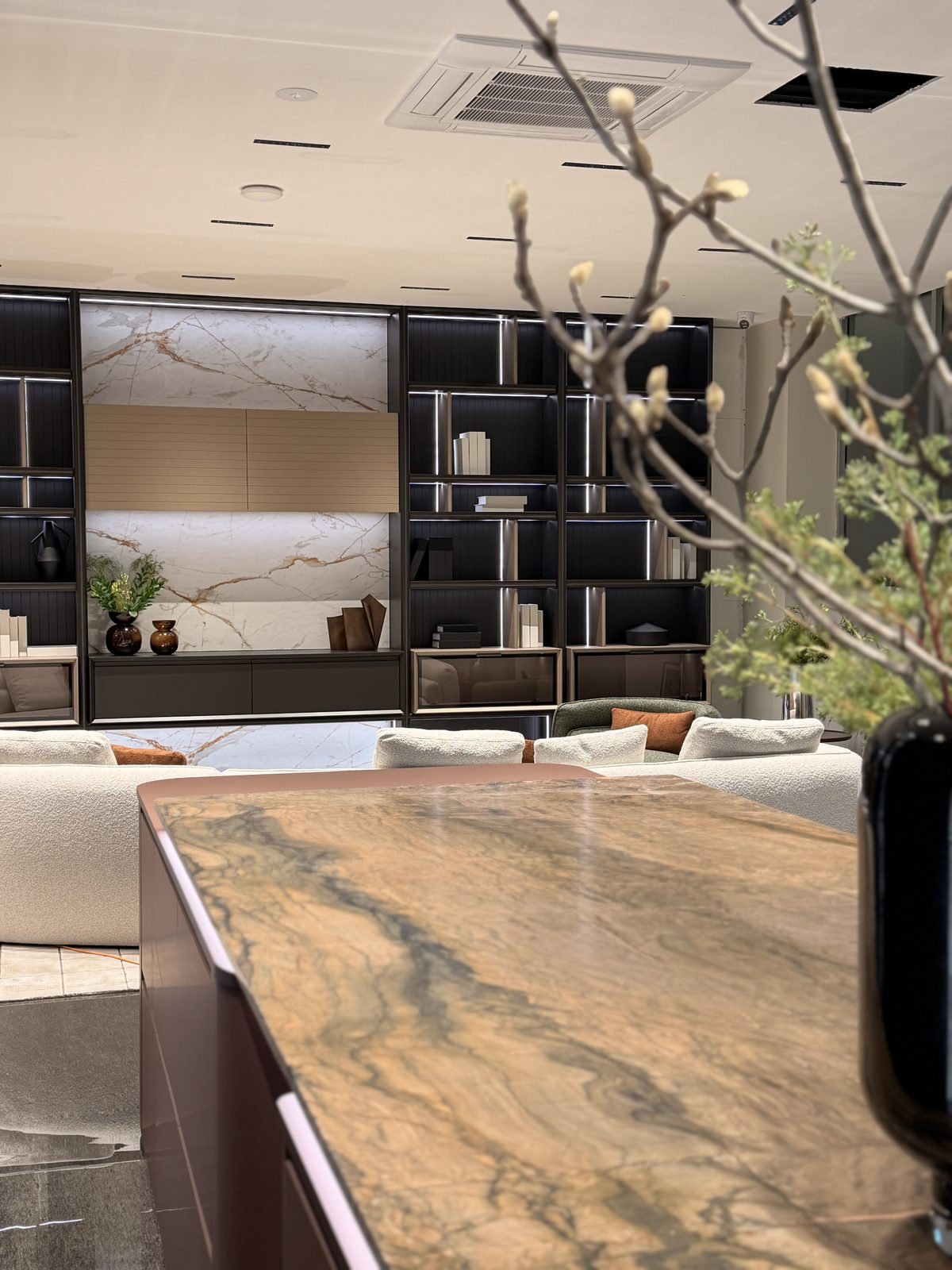 Retail showroom lounge display in Cremorne after an end-of-build clean, with a stone-top island bench in the foreground, dark shelving wall with marble feature panel and cream sofas