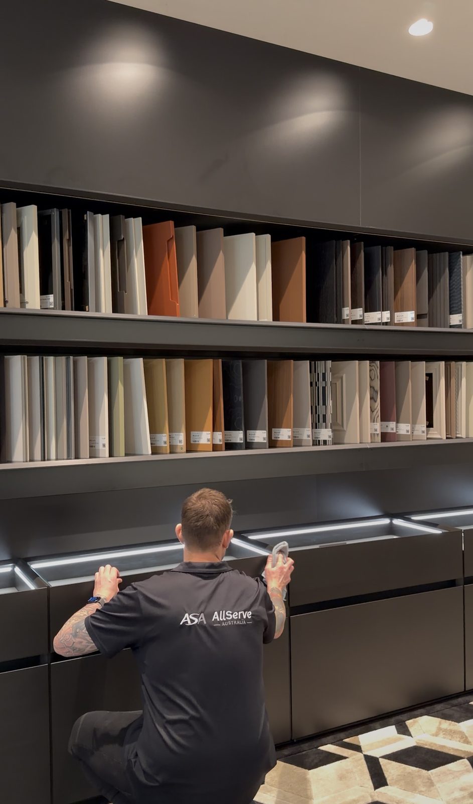Cleaner wiping display drawers beneath shelves of joinery and finish samples in the showroom