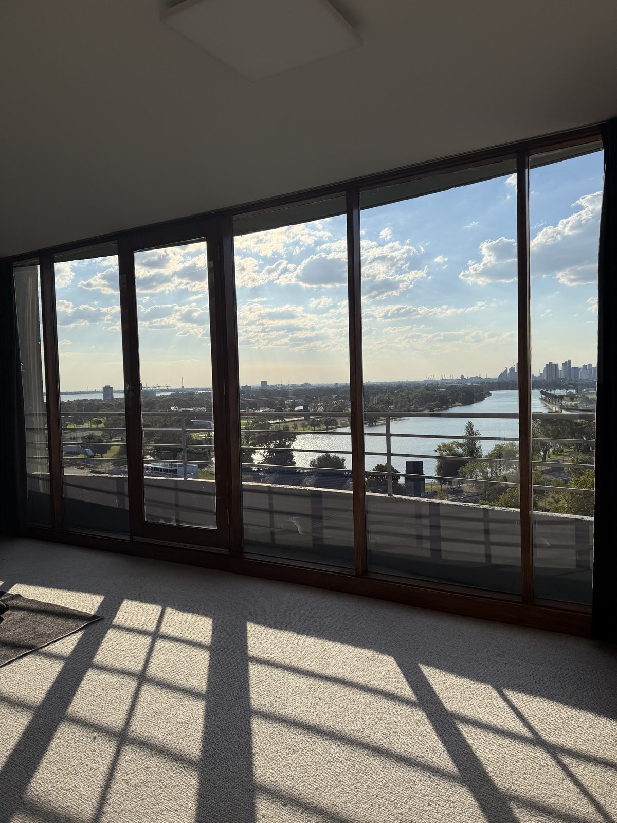 Empty carpeted room in a St Kilda apartment with sunlight streaming through freshly cleaned floor-to-ceiling windows and a clear view over the water.