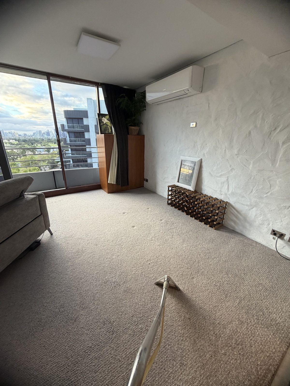 Carpet steam cleaning in progress in a St Kilda apartment living room, with the cleaning wand in the foreground and fresh wand strokes visible across the carpet.