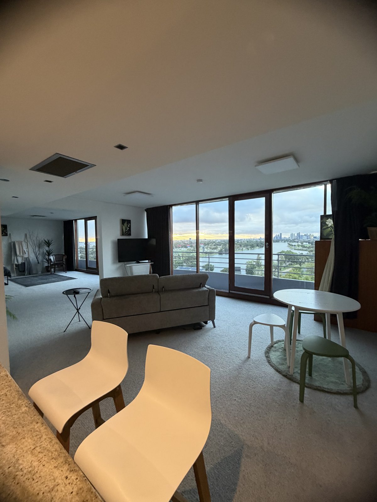 Open-plan living area of a St Kilda apartment after an end of lease clean, with freshly cleaned carpet, sofa and dining setting, and floor-to-ceiling windows overlooking a lake and the city skyline.
